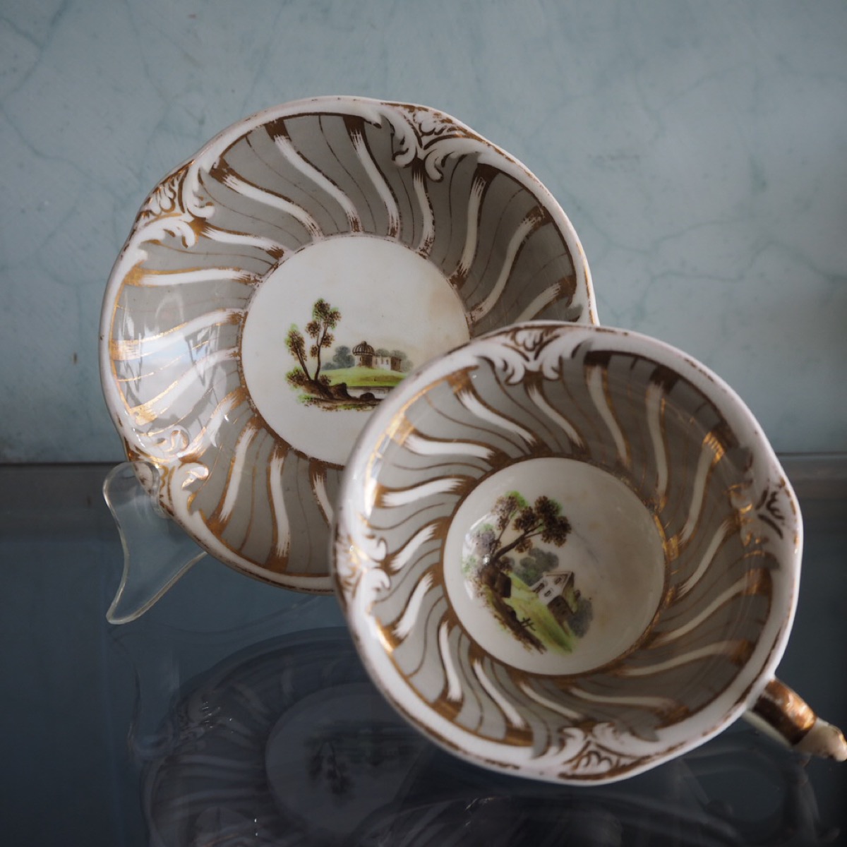 Rockingham cup & saucer with central village scene, surrounded by wide grey and gilt rococo border, c. 1830